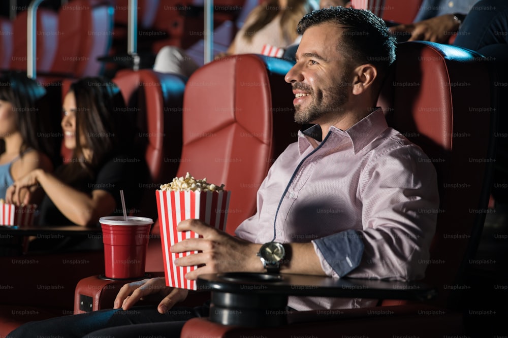 Vista di profilo di un bel giovane che mangia popcorn e guarda un film da solo al teatro