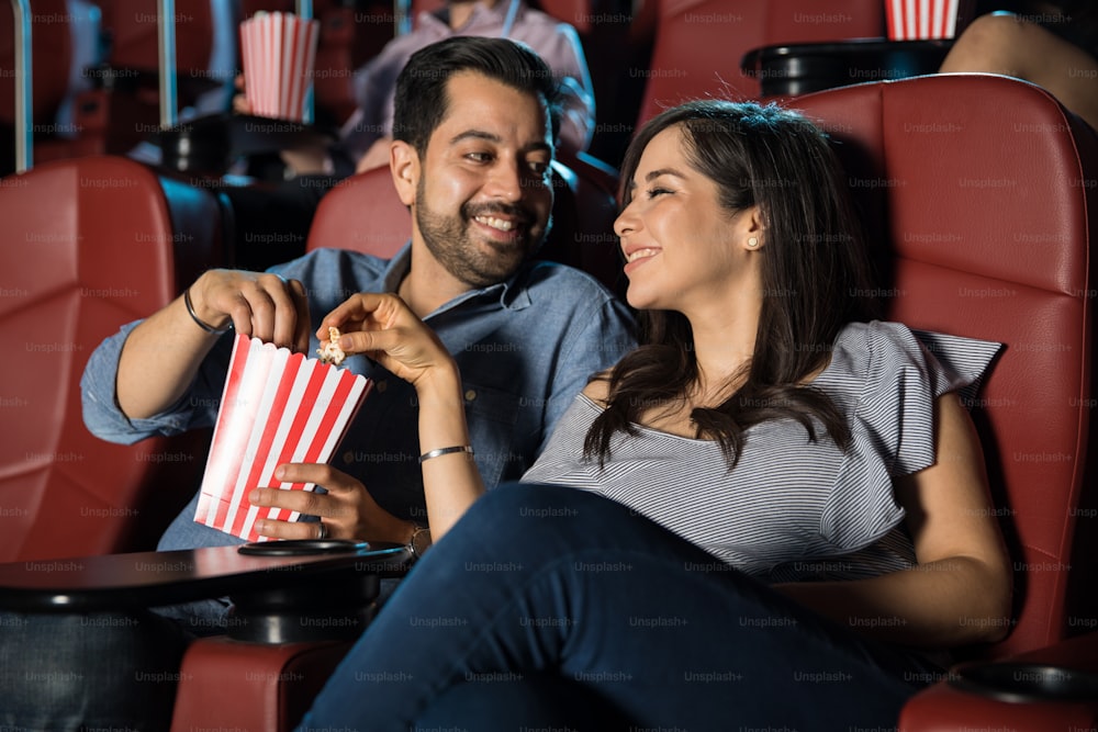 Feliz pareja hispana viendo una película en el cine y compartiendo unas palomitas de maíz
