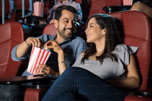 Feliz pareja hispana viendo una película en el cine y compartiendo unas palomitas de maíz