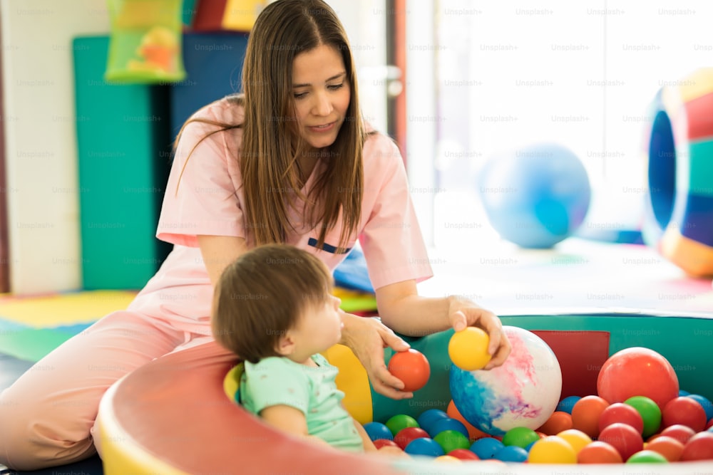 어린이 치료 센터의 볼 풀장에서 아기와 놀고 있는 매력적인 여성 치료사