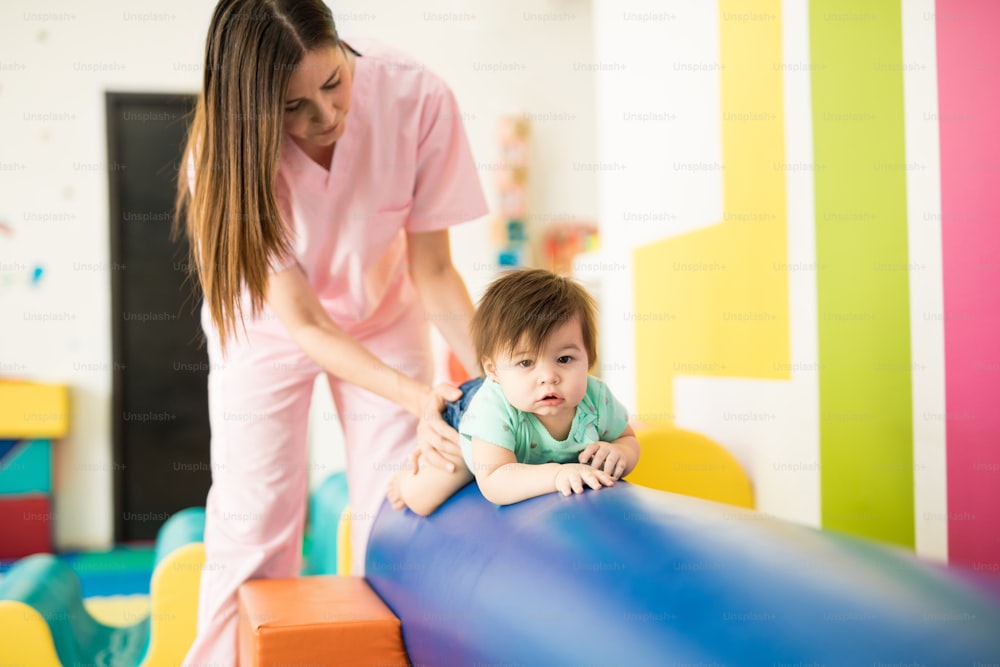 Hispanic baby crawling on a beam and practicing balance with the help of a therapist