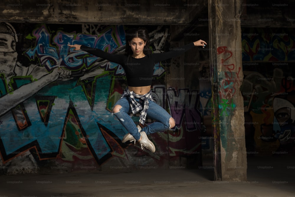 Porträt einer hübschen Tänzerin, die vor einer Graffiti-Wand springt und Blickkontakt herstellt