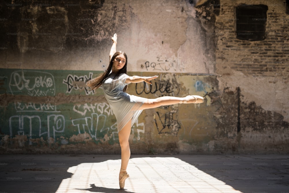 Pretty and talented female dancer performing a dance routine in an urban setting with graffiti walls