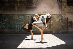 Wunderschönes Paar Tänzerinnen, die zusammen und synchronisiert im Freien in einer urbanen Umgebung auftreten