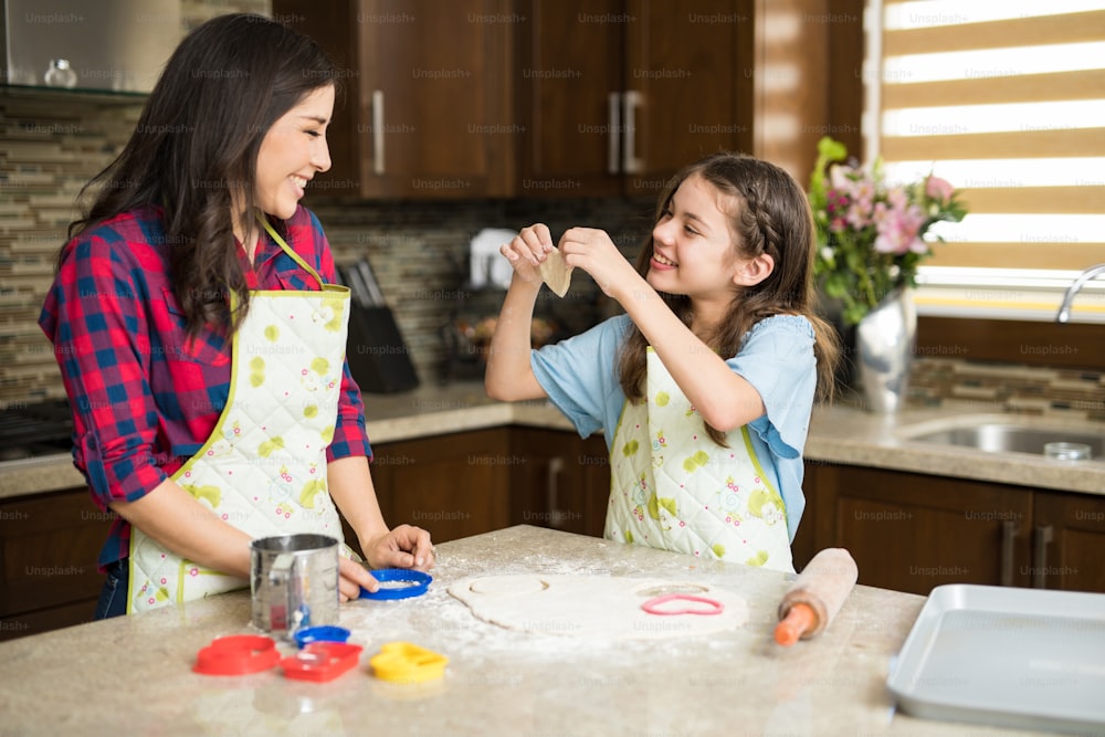 Bella ragazza che taglia un biscotto a forma di cuore e lo mostra a sua madre in cucina