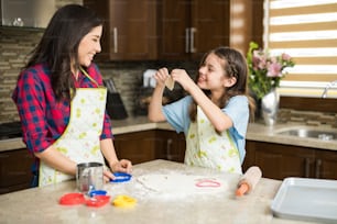 Hübsches Mädchen, das einen Keks in Form eines Herzens schneidet und ihn ihrer Mutter in der Küche zeigt