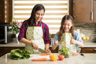 Happy mother and daughter making a salad for dinner together at home