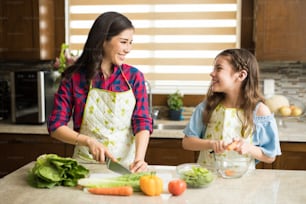 Pretty young mother and daughter chopping and peeling vegetables for a salad at home