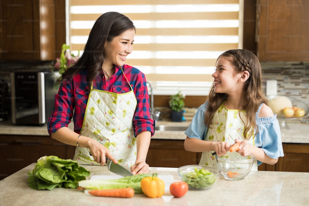 Bella giovane madre e figlia che tagliano e sbucciano le verdure per un'insalata a casa