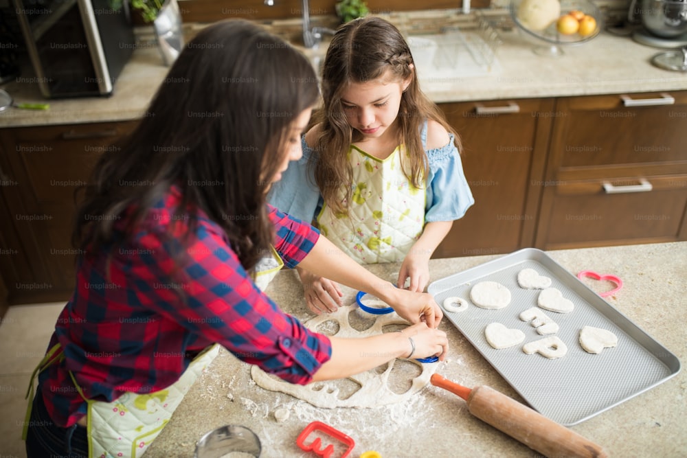 Vista dall'alto di una giovane madre e sua figlia che cuociono insieme e tagliano la pasta per biscotti in diverse forme