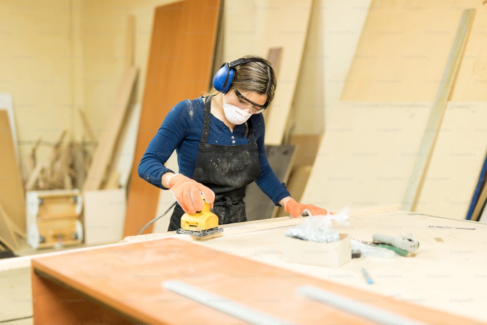 Portrait of a good looking female carpenter sanding some wood in a workshop