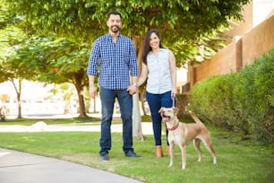 Portrait of a beautiful Hispanic couple going for a walk at a park with their friendly dog and smiling