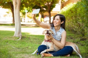 Wunderschöne junge Frau und ihr freundlicher Hund, der ein Selfie mit einem Smartphone in einem Park macht