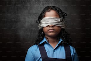 Portrait clair et ombragé d’une écolière aux yeux bandés dans un arrière-plan sombre