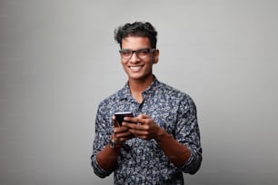 Smiling young man of Indian origin holding a mobile phone in his hand