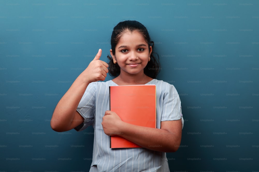 Happy young girl holding note books in her hand shows thumbs up sign