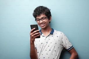 Lächelnder Junge indischer Herkunft schaut auf sein Handy