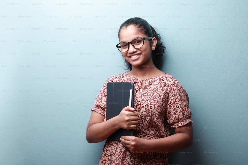 Retrato de una niña sonriente de etnia india sosteniendo una tableta en la mano