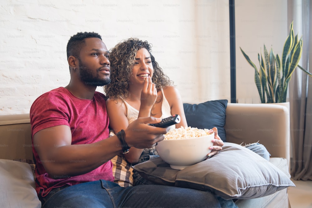 Young couple spending time together and watching tv series or movies while sitting on couch at home.