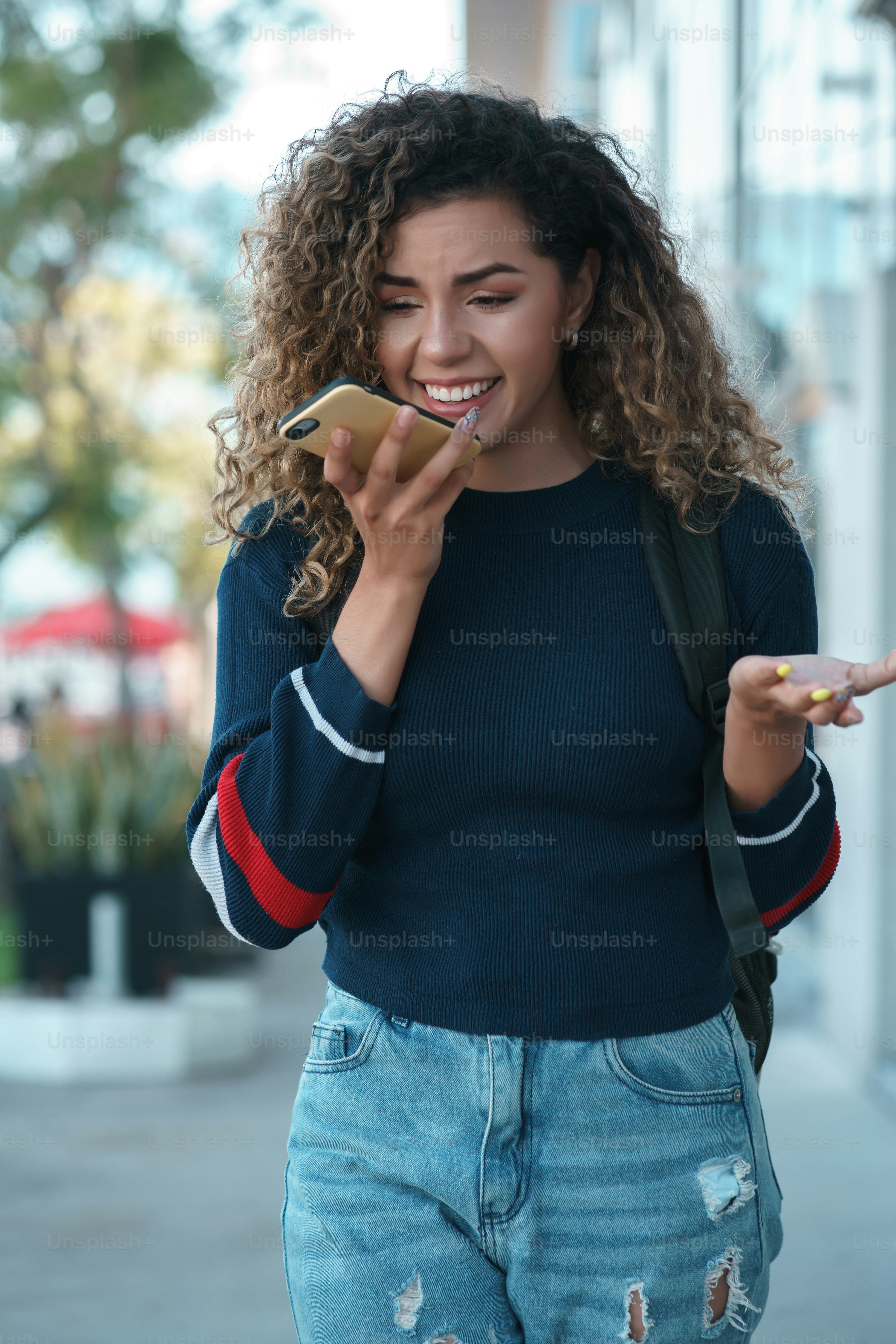 Young latin woman sending a voice message on her mobile phone while walking outdoors on the street. Urban concept.