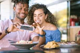 Young couple using a mobile phone and taking photos to the food while having lunch together at a restaurant.
