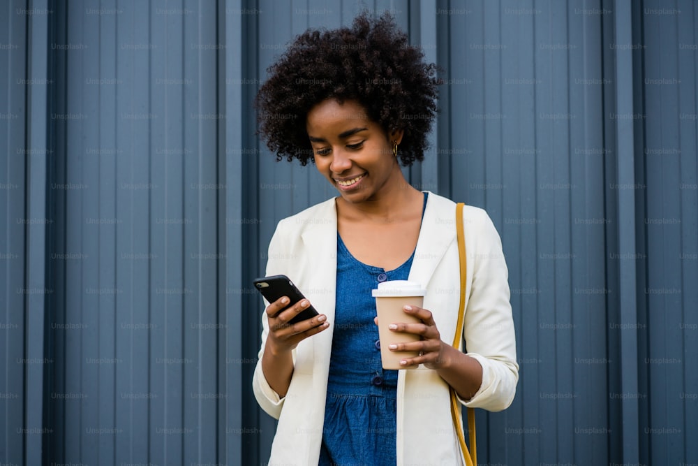 Retrato de una mujer de negocios afro usando su teléfono móvil mientras está parada al aire libre en la calle. Concepto empresarial y urbano.