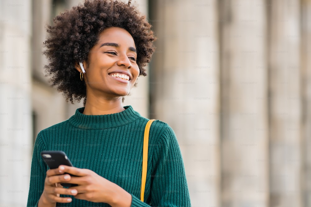 Retrato de una mujer de negocios afro usando su teléfono móvil mientras está parada al aire libre en la calle. Concepto empresarial y urbano.