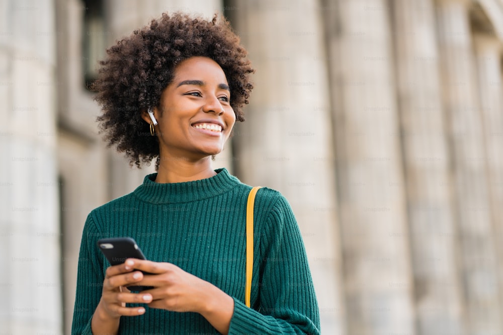 Portrait of afro business woman using her mobile phone while standing outdoors at the street. Business and urban concept.