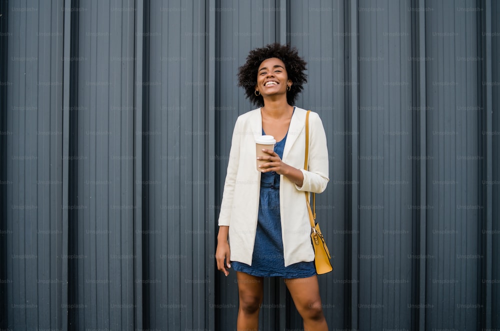 Retrato de una mujer de negocios afro sosteniendo una taza de café mientras está parada al aire libre en la calle. Concepto empresarial y urbano.