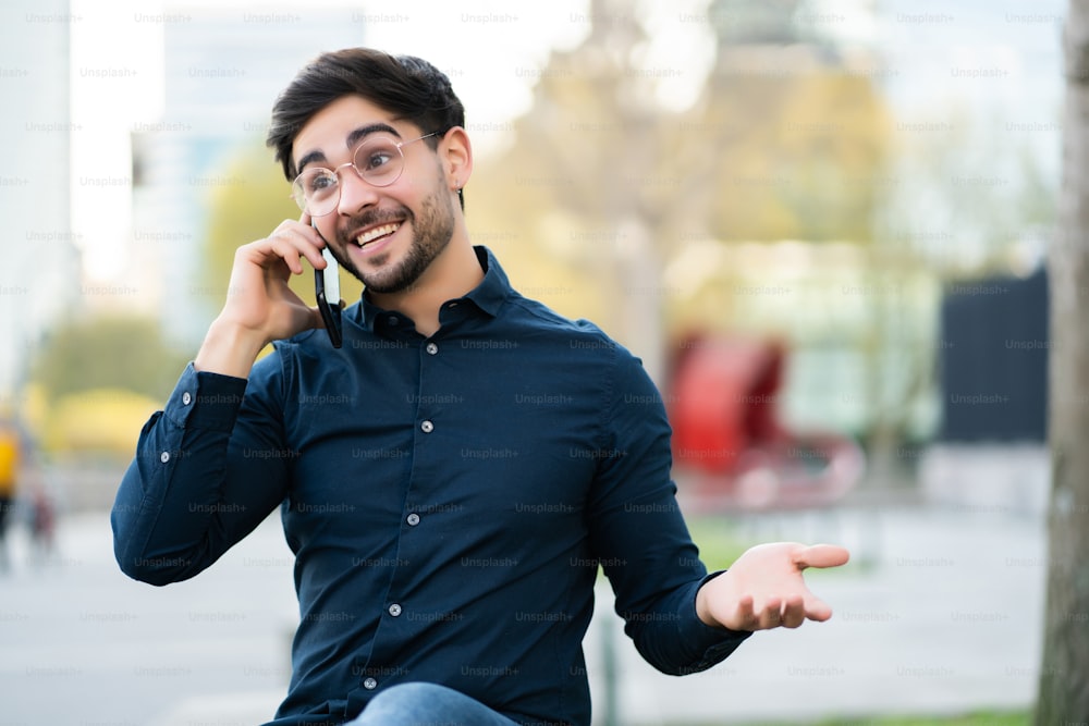 Portrait of young man talking on the phone while sitting on bench outdoors. Urban concept.