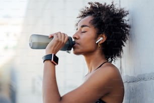 Afro donna atletica che beve acqua e si rilassa dopo l'allenamento all'aperto. Sport e stile di vita sano.