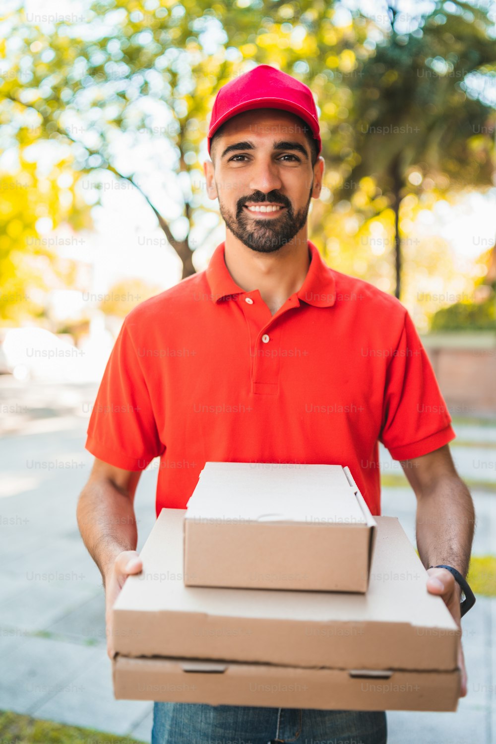 Retrato de un repartidor con una caja de pizza de cartón al aire libre en la calle. Concepto de servicio de entrega y envío.