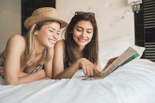 Portrait of two young travelers friends spending some time and organizing their trip at hotel room. Travel and lifestyle concept.