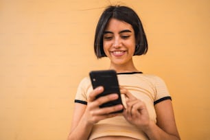 Portrait of young latin woman using her mobile phone outdoors in the street. Urban and communication concept.