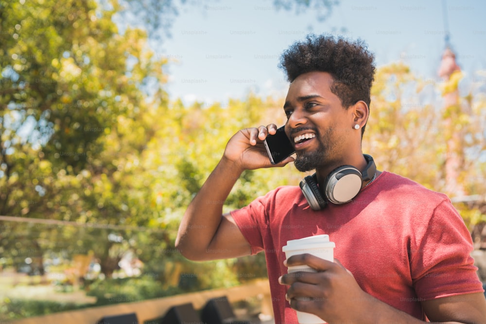 Portrait of young afro man talking on the phone while holding a cup of coffee outdoors. Communication, lifestyle and urban concept.
