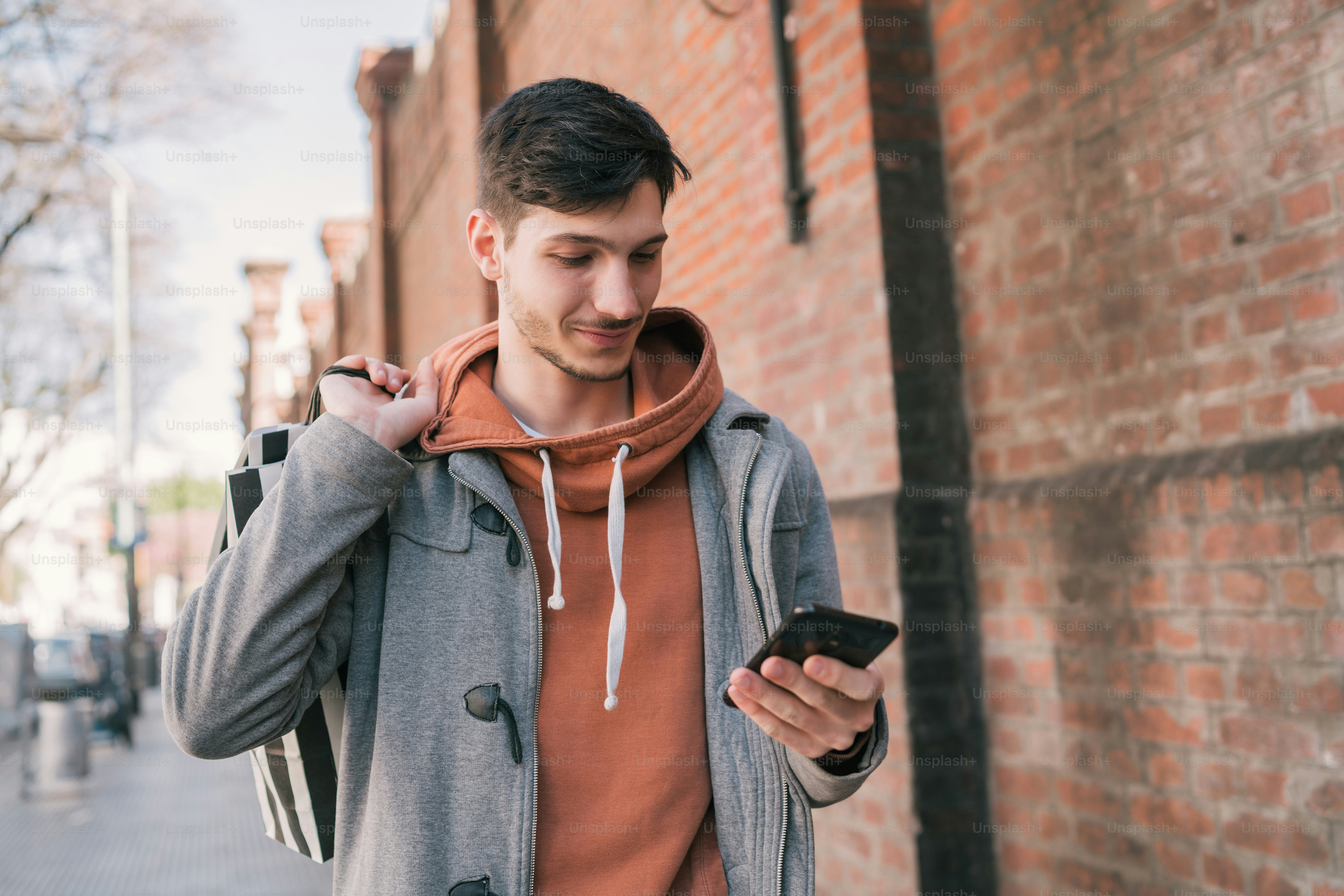Portrait of young handsome man walking on the street, holding shopping bags and using his mobile phone. Urban, shop concept.