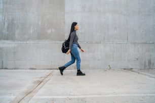 Portrait of young beautiful Asian woman walking against grey concrete wall.