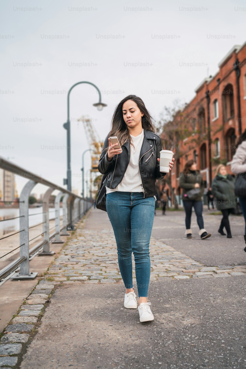 Retrato de una mujer joven usando su teléfono móvil mientras camina con una taza de café. Concepto urbano y de comunicación.