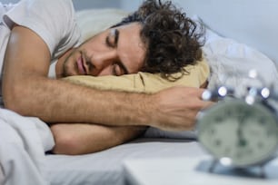 Young latin man sleeping with alarm clock. Indoors.