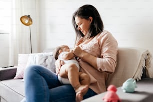 自宅のソファで赤ちゃんに母乳を与える母親