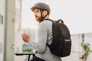 Giovane adulto in piedi sulla bicicletta usando lo smartphone in città