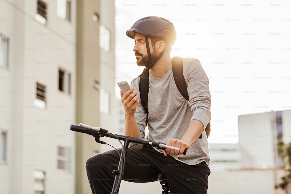 Young adult standing on bicycle using smartphone in the city