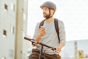 Cyclist standing looking at his smartphone in the city. Concept of using gps map or delivery apps