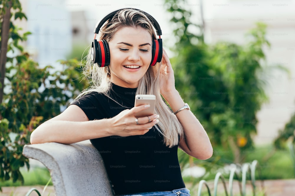 Femme écoutant la musique d’un téléphone intelligent avec des écouteurs dans un parc