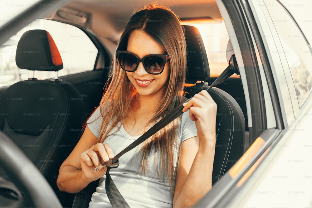 Mulher de óculos escuros prendendo um cinto de segurança no carro.