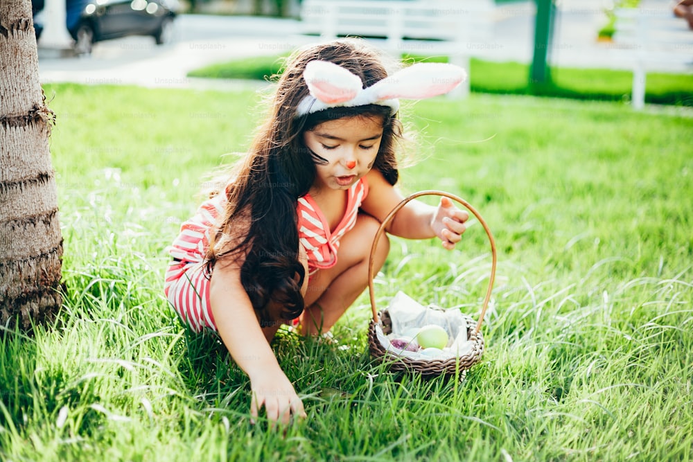 庭にウサギの耳とイースターエッグのバスケットを持つかわいい女の子。イースターエッグハント