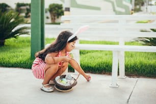 Cute little girl with bunny ears and basket of Easter eggs in the garden. Easter egg hunt