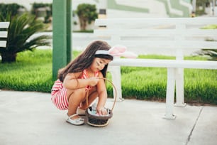 Cute little girl with bunny ears and basket of Easter eggs in the garden. Easter egg hunt