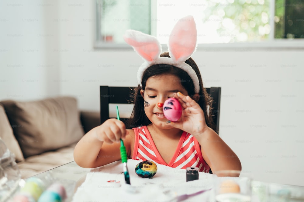 Joyeuses Pâques! Une belle fille d’enfant peignant des œufs de Pâques. Famille heureuse se préparant pour Pâques. Mignonne petite fille portant des oreilles de lapin le jour de Pâques