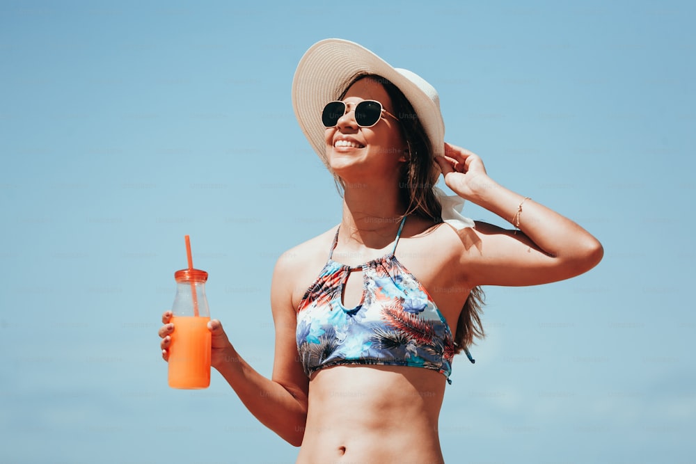Mulher da moda que bebe o coquetel na praia